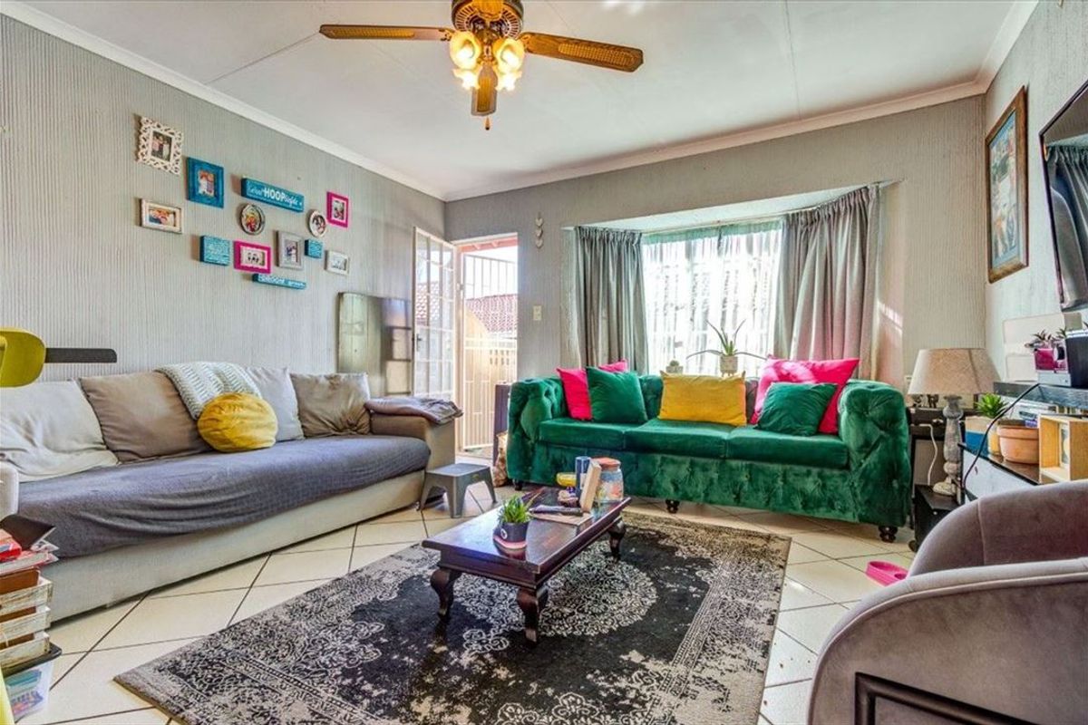 A comfortable living room featuring tiled flooring, a ceiling fan, and a large bay window that allows for natural light.