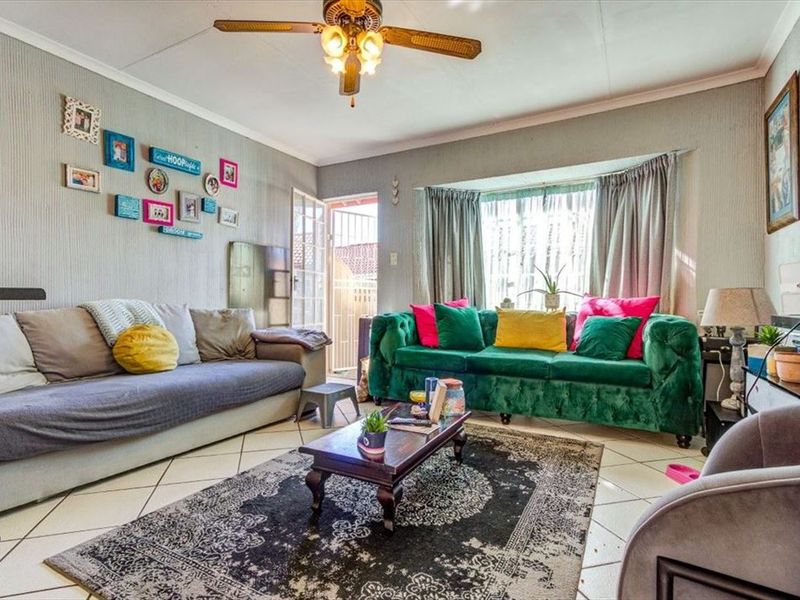 A comfortable living room featuring tiled flooring, a ceiling fan, and a large bay window that allows for natural light.