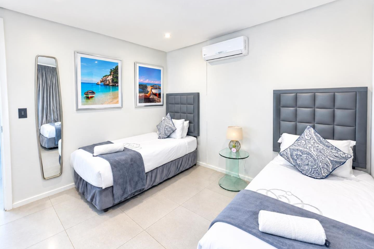 A well-maintained bedroom featuring neutral tiled flooring, recessed downlighting, and a wall-mounted split-system air conditioning unit.