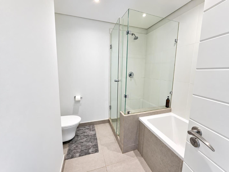Modern bathroom featuring a glass-enclosed shower, a built-in bathtub, and a wall-mounted toilet with neutral tiled finishes.