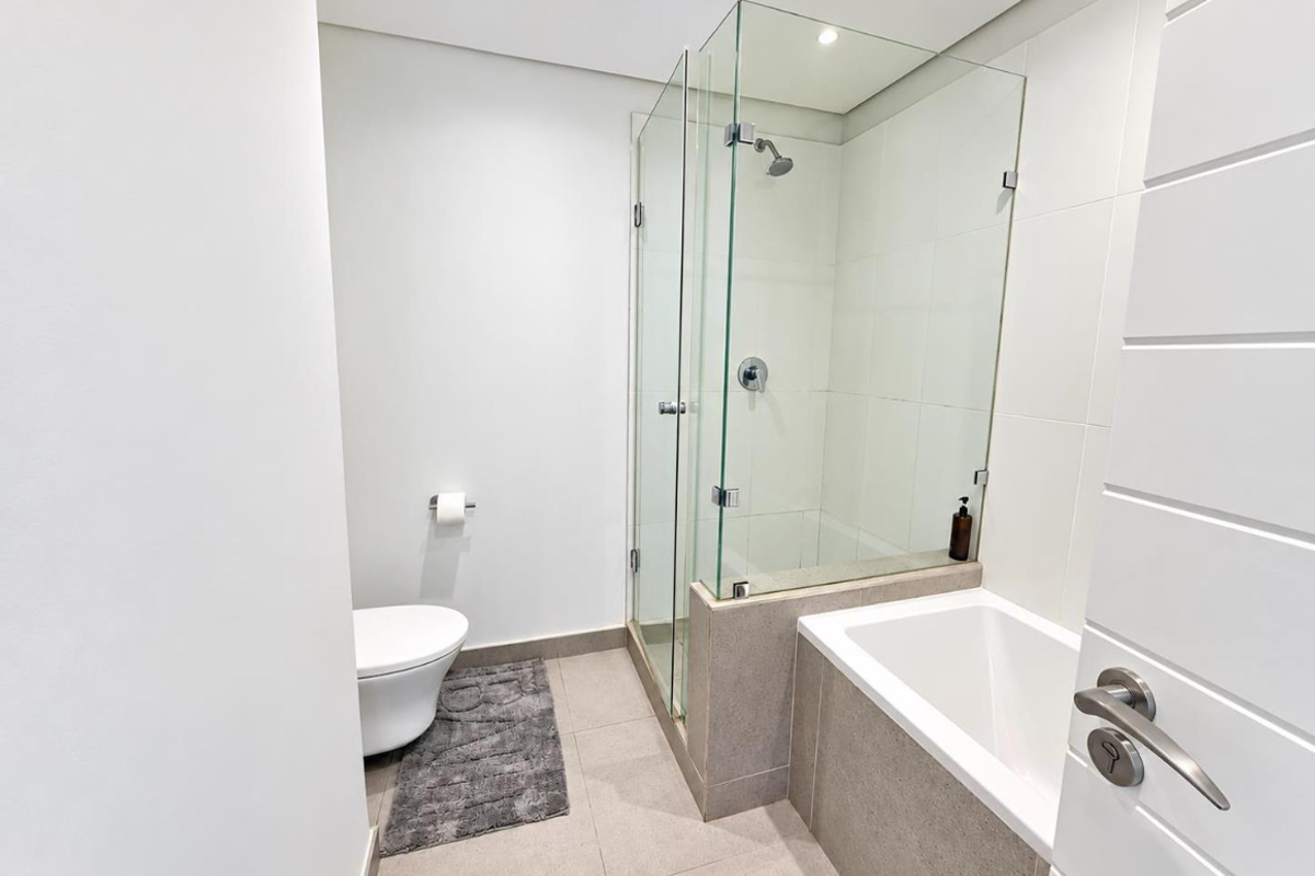 Modern bathroom featuring a glass-enclosed shower, a built-in bathtub, and a wall-mounted toilet with neutral tiled finishes.