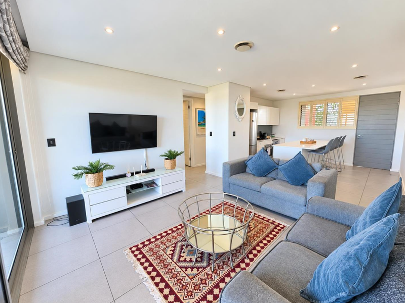 Spacious open-plan living and kitchen area featuring modern tiled flooring, recessed lighting, and a functional kitchen island with integrated cabinetry.