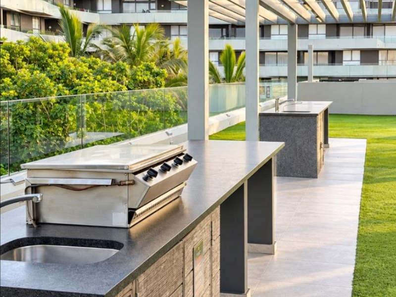 Outdoor entertainment area featuring a built-in braai, granite countertops, stainless steel sink, and a modern pergola overlooking the complex garden.