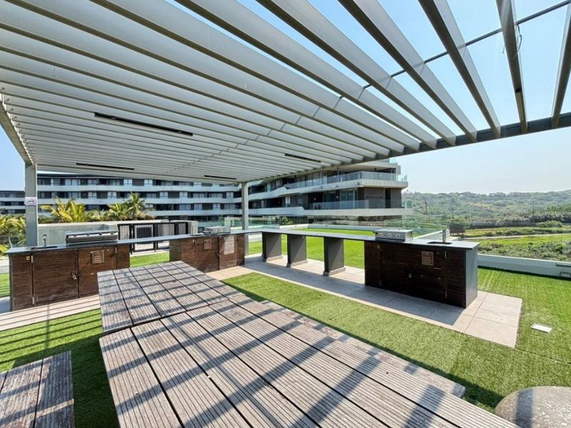 Spacious outdoor patio area featuring a modern pergola, built-in braai facilities, and a sleek kitchen counter, perfect for entertaining with scenic views.