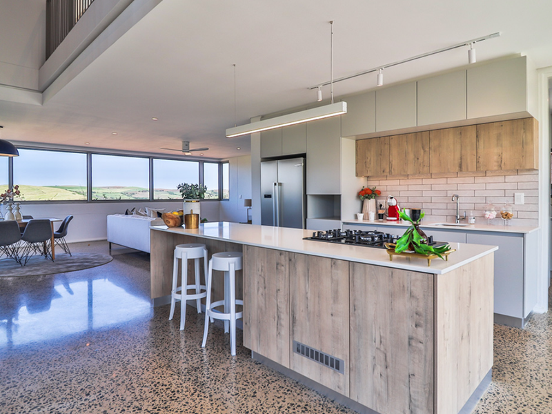Modern open-plan kitchen and living area featuring a large island, polished concrete floors, and expansive windows with scenic views.