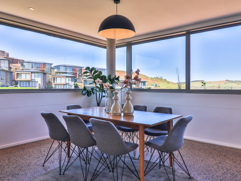 Modern dining area featuring expansive corner windows with panoramic views, polished concrete floors, and contemporary recessed and pendant lighting.