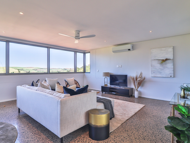 Modern living room featuring polished concrete floors, large windows with scenic views, recessed lighting, and a wall-mounted split-system air conditioner.