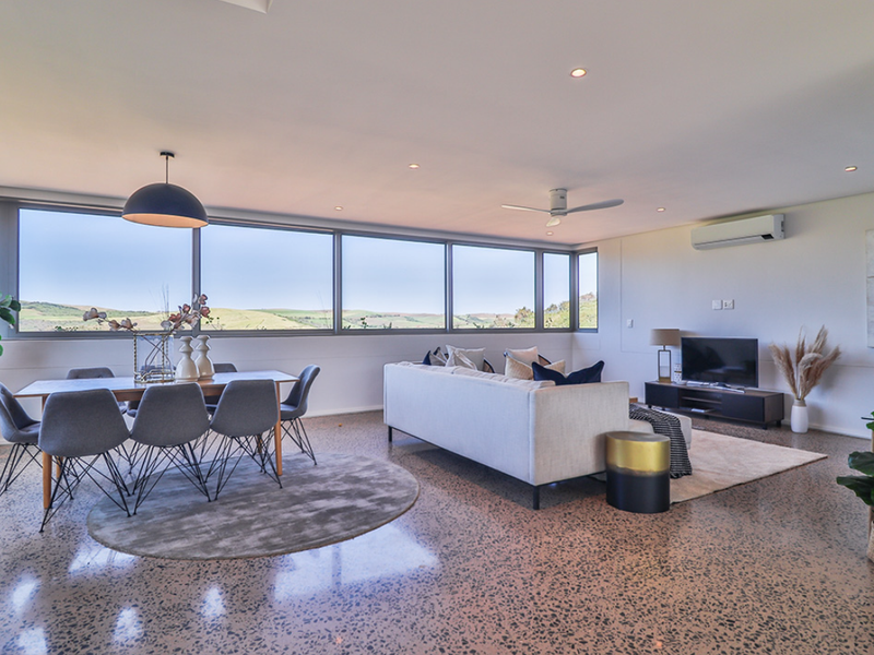 Spacious open-plan living and dining area featuring polished concrete floors, recessed lighting, and expansive windows offering scenic landscape views.