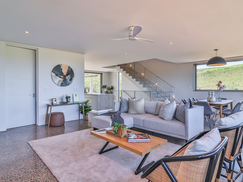 Spacious open-plan living and dining area featuring polished concrete floors, modern staircase, and large windows with scenic views.