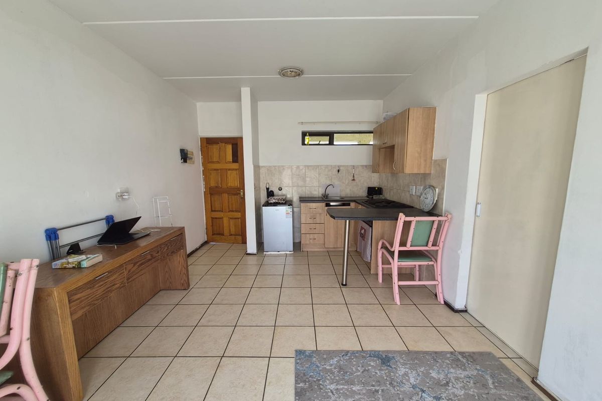 Open plan living area featuring a compact kitchen with built-in cabinetry, breakfast bar, and tiled flooring throughout.