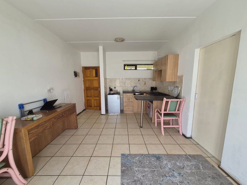 Open plan living area featuring a compact kitchen with built-in cabinetry, breakfast bar, and tiled flooring throughout.