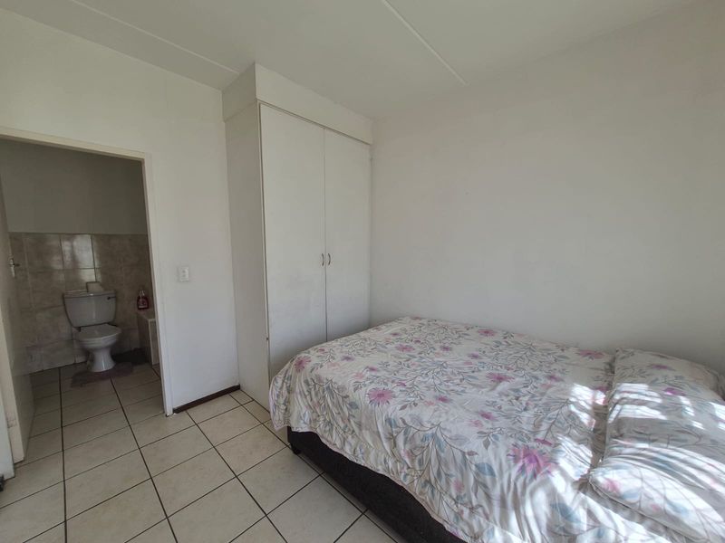 A bedroom featuring tiled flooring and a built-in wardrobe, with an adjoining bathroom visible through the doorway.