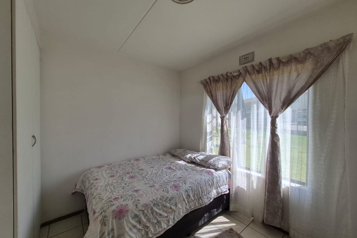 A functional bedroom featuring tiled flooring, a built-in wardrobe, and natural light through a large window.