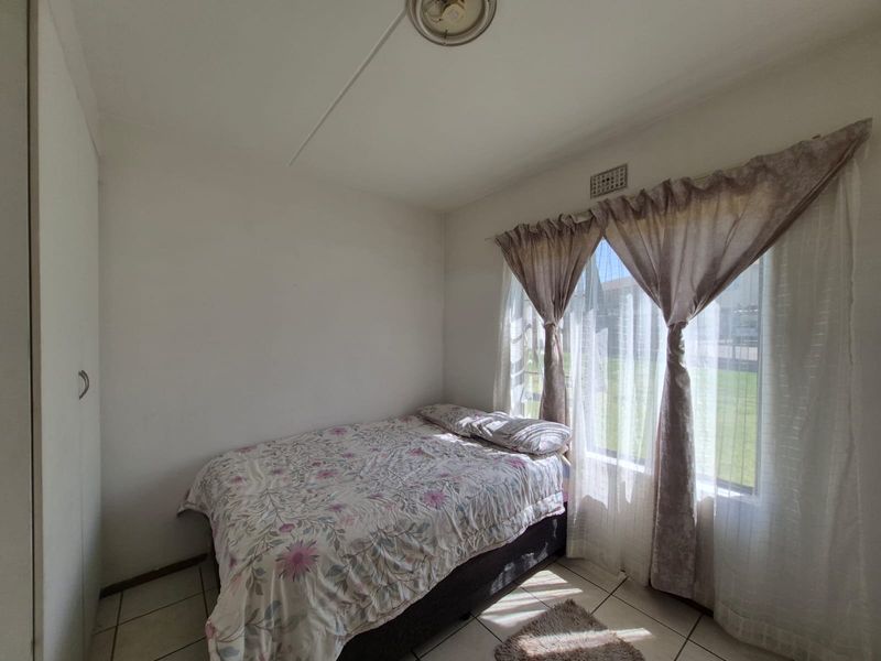 A functional bedroom featuring tiled flooring, a built-in wardrobe, and natural light through a large window.