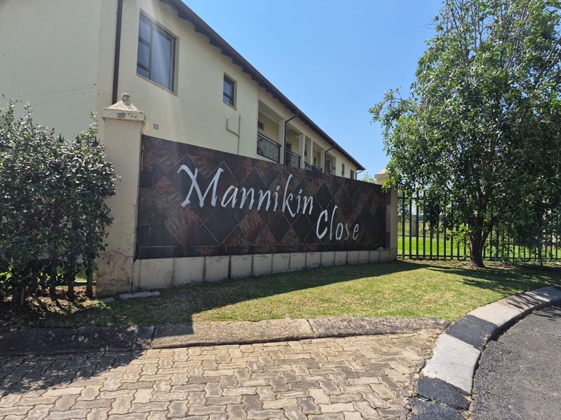 Exterior view of the Mannikin Close apartment complex entrance, featuring signage, paved driveway, and perimeter fencing.