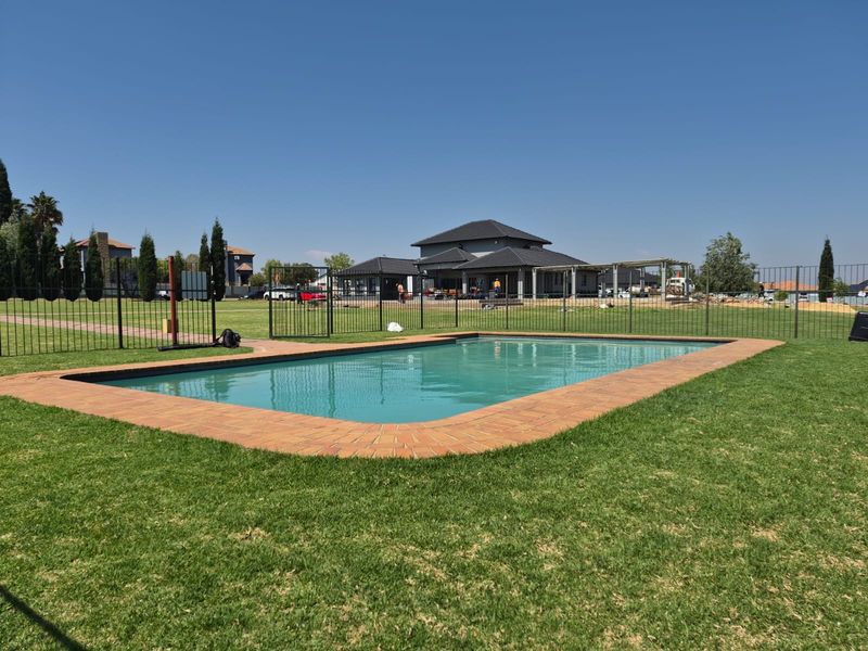 A well-maintained outdoor swimming pool area featuring brick coping and secure metal perimeter fencing set within a spacious grassed garden.