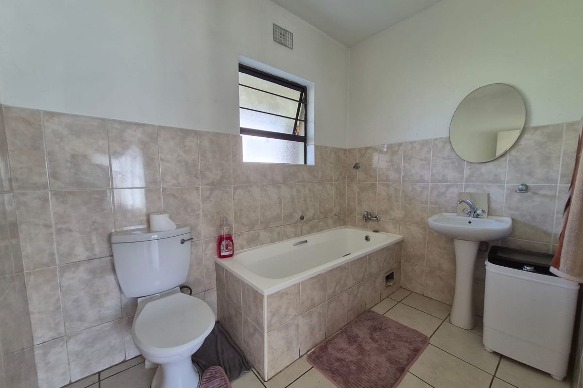 A functional bathroom featuring a pedestal basin, built-in bathtub, and neutral ceramic tiling throughout.