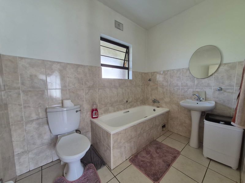 A functional bathroom featuring a pedestal basin, built-in bathtub, and neutral ceramic tiling throughout.