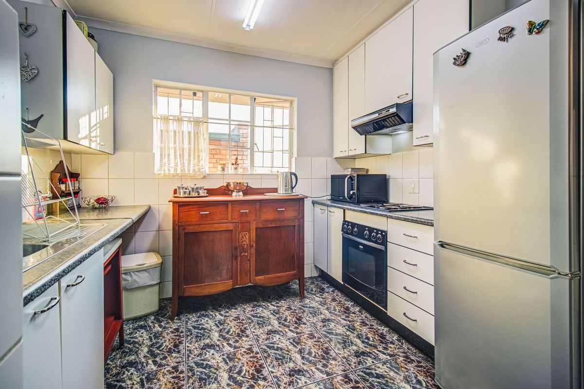 A functional kitchen featuring built-in cabinetry, a built-in oven with hob, extractor fan, and tiled splashbacks, with a window providing natural light.