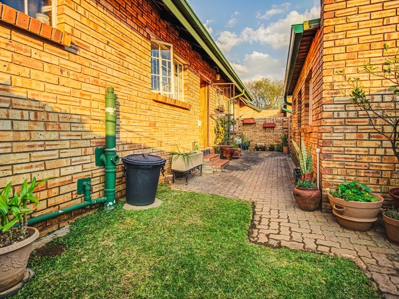 A rear exterior view of a townhouse featuring face brick walls, a paved walkway, and established garden elements along the side of the building.