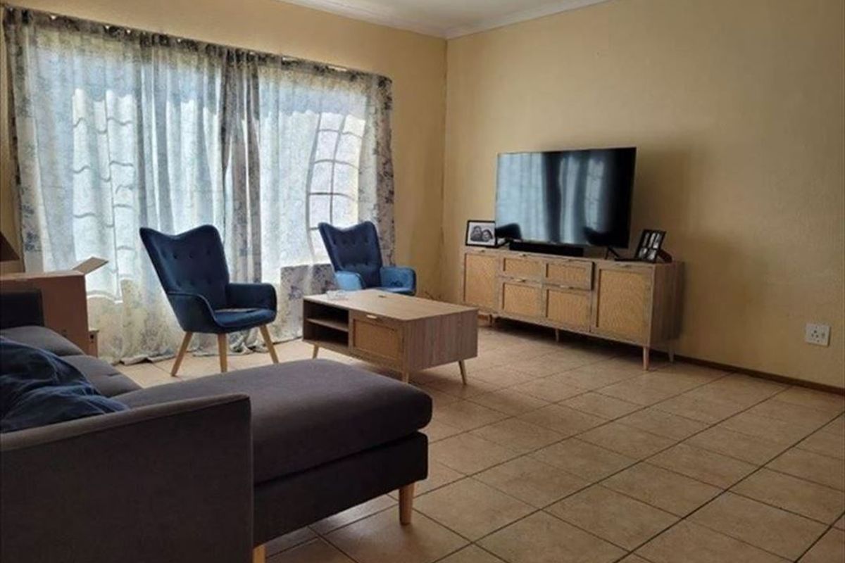 A living room featuring tiled flooring and large windows with curtain tracks, providing a functional and well-lit space.