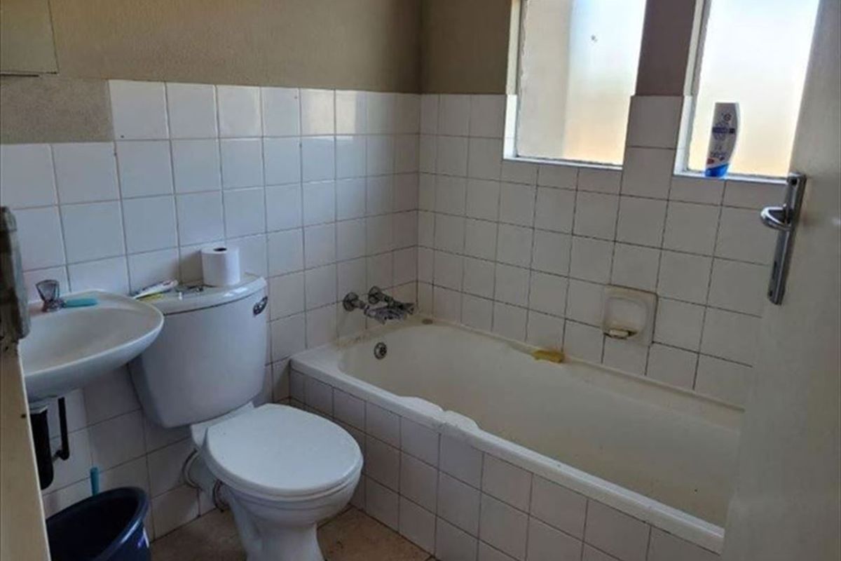 A functional bathroom featuring a bathtub, toilet, and pedestal basin with tiled finishes, requiring cosmetic updates to improve its overall condition.