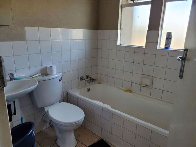 A functional bathroom featuring a bathtub, toilet, and pedestal basin with tiled finishes, requiring cosmetic updates to improve its overall condition.