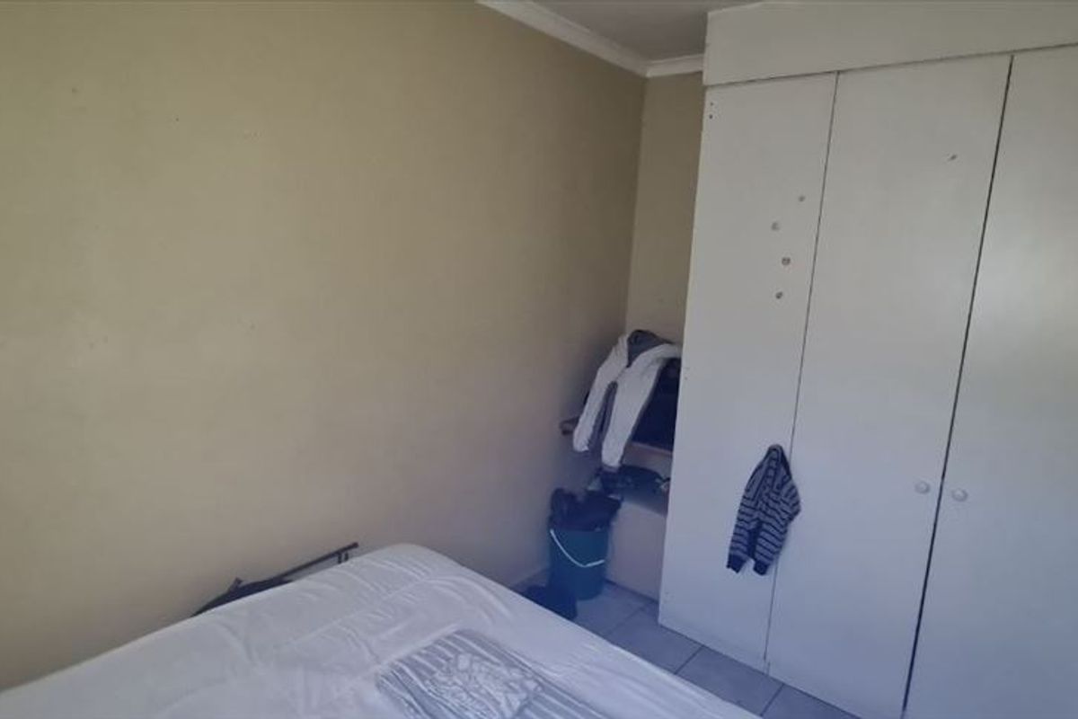 A bedroom featuring tiled flooring and a built-in wardrobe, requiring cosmetic updates to the wall finishes and cabinetry.