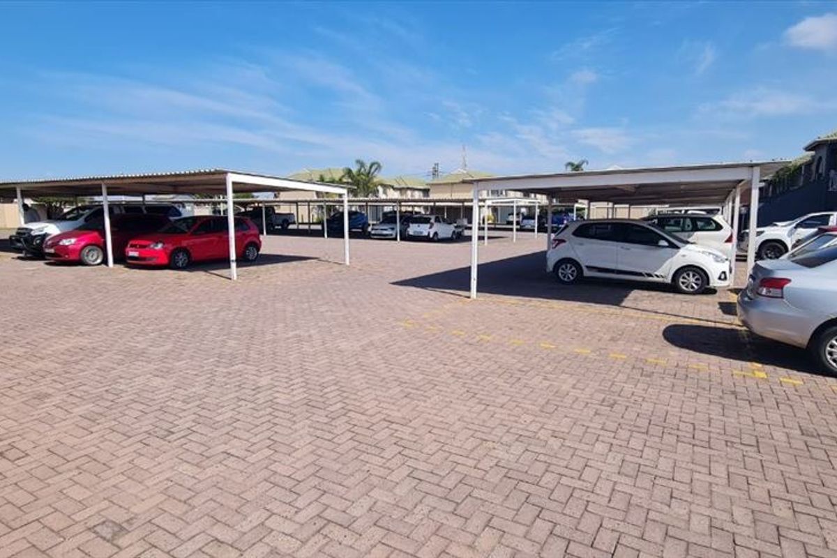 An outdoor parking area featuring multiple covered parking bays with metal structures and paved ground surfaces within an apartment complex.