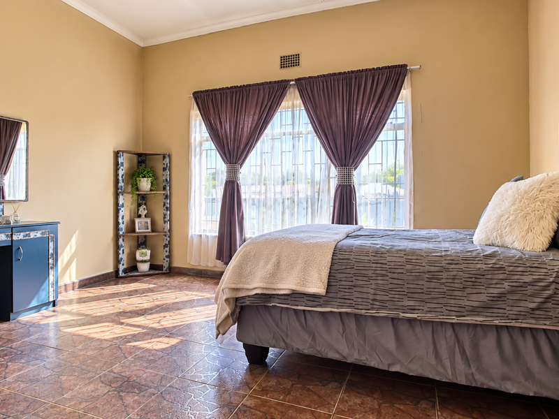A spacious bedroom featuring tiled flooring, large windows with security bars, and neutral wall finishes, providing a comfortable and well-lit living space.