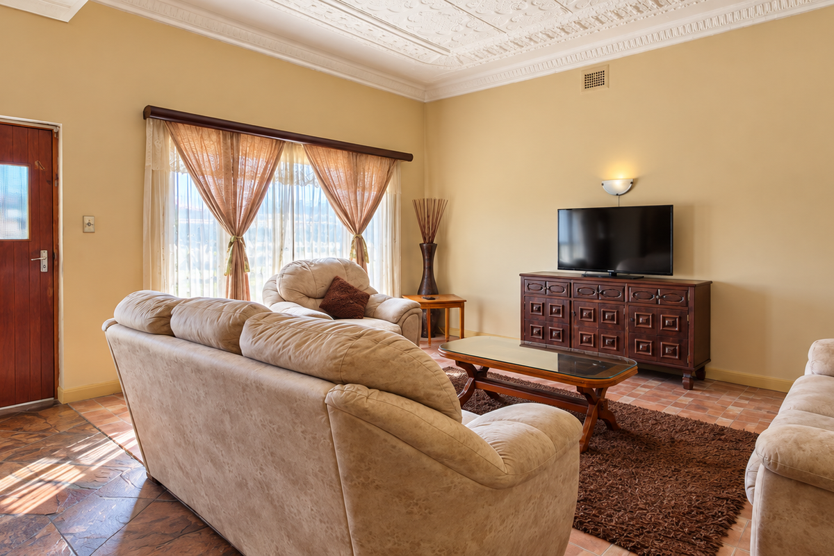 A spacious living room featuring classic terracotta tile flooring, an ornate decorative plaster ceiling, and a solid timber entrance door.