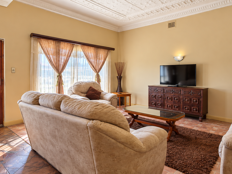 A spacious living room featuring classic terracotta tile flooring, an ornate decorative plaster ceiling, and a solid timber entrance door.