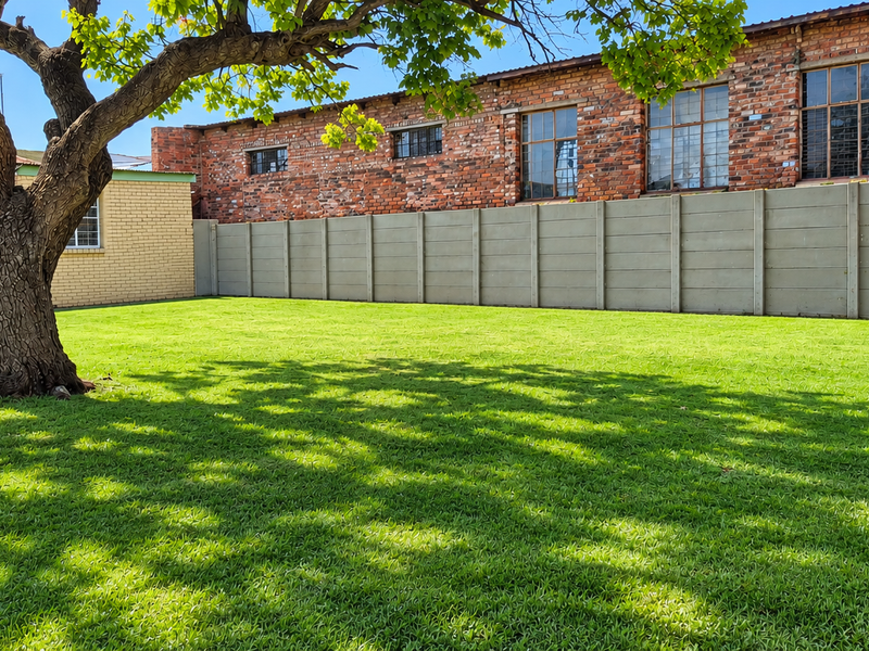 A spacious, well-maintained private garden featuring a large mature tree, lush green lawn, and secure precast concrete boundary walling.