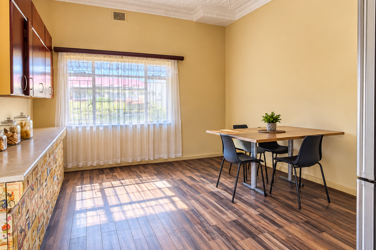 A functional kitchen area featuring laminate flooring, built-in cabinetry with decorative finishes, and a dining space illuminated by natural light from a large window.