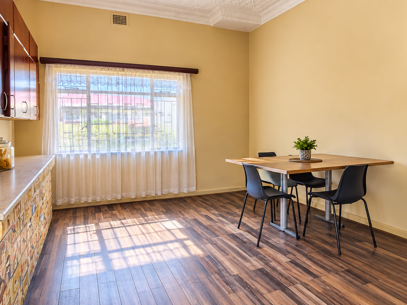 A functional kitchen area featuring laminate flooring, built-in cabinetry with decorative finishes, and a dining space illuminated by natural light from a large window.