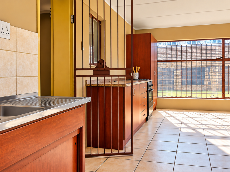 A functional kitchen featuring built-in wooden cabinetry, a double stainless steel sink, and tiled flooring, with large windows secured by metal bars.