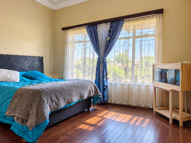 A well-lit bedroom featuring polished hardwood flooring, crown molding, and large windows fitted with security bars.