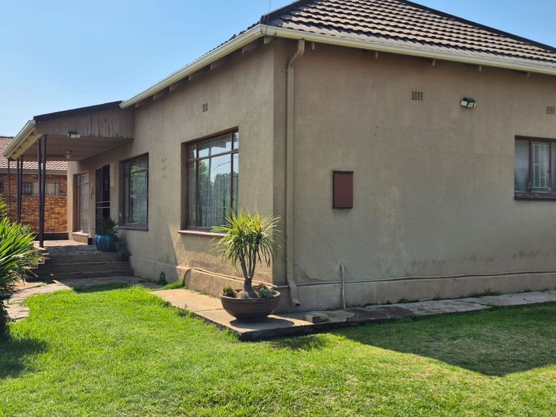 Rear view of a single-story house featuring a tiled roof, plastered exterior walls, and a small covered patio area with a surrounding garden.
