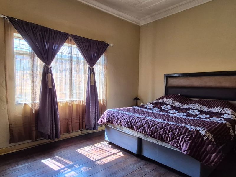 A bedroom featuring original hardwood flooring, ornate ceiling cornicing, and security bars on the window. The space requires cosmetic updates to wall finishes.