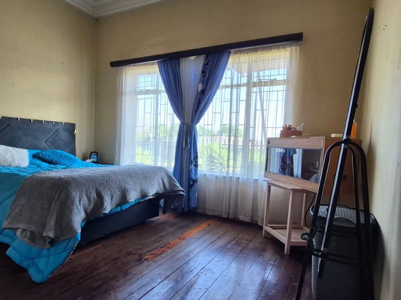 A bedroom featuring original hardwood flooring, large windows with security bars, and decorative cornice detailing, requiring cosmetic updates to the walls and finishes.