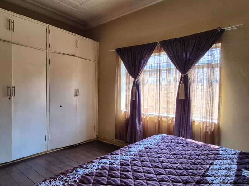 A bedroom featuring timber flooring, ornate ceiling cornices, and extensive built-in cupboard storage, requiring cosmetic updates to modernize the space.