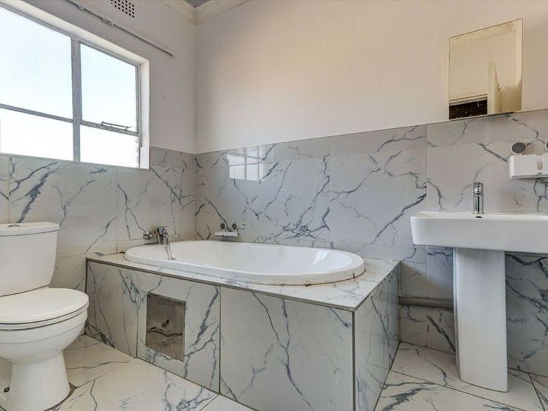 A functional bathroom featuring a built-in bathtub, pedestal basin, and toilet, finished with marble-look wall and floor tiles.