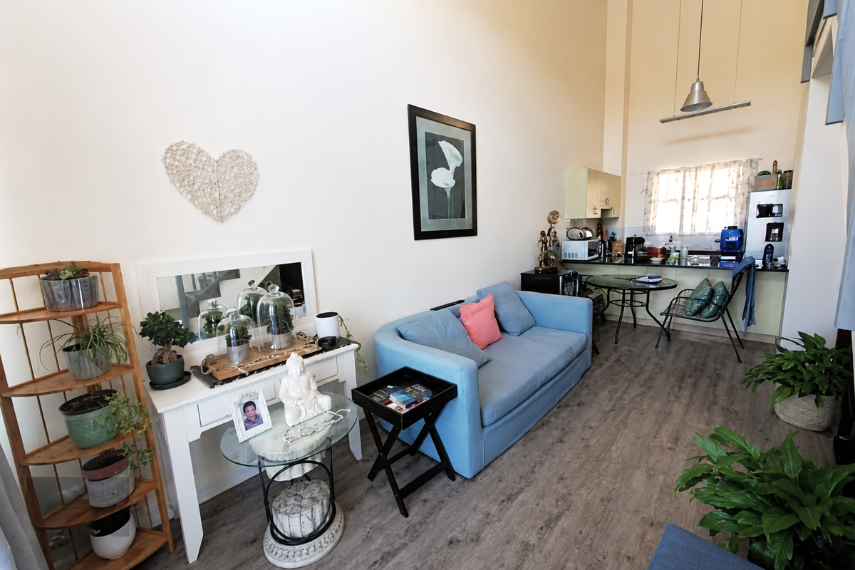 Open-plan living area featuring high ceilings, laminate flooring, and a compact kitchen with built-in cabinetry and countertop space.