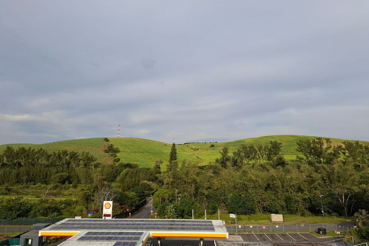 Elevated view overlooking a petrol station with solar panels, surrounded by lush green hills and natural landscape.