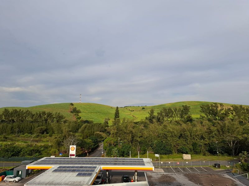 Elevated view overlooking a petrol station with solar panels, surrounded by lush green hills and natural landscape.