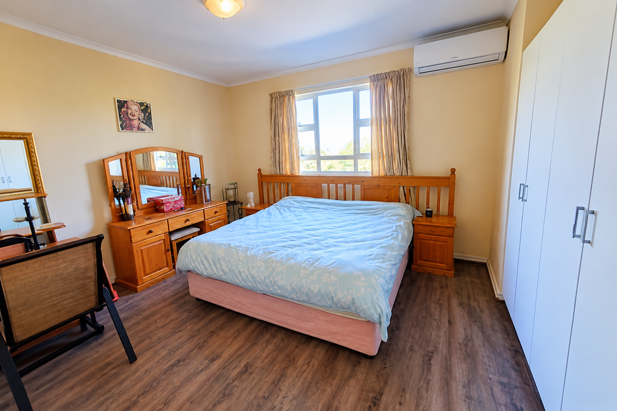 A well-maintained bedroom featuring laminate flooring, a built-in wardrobe, and a wall-mounted split-system air conditioner for climate control.