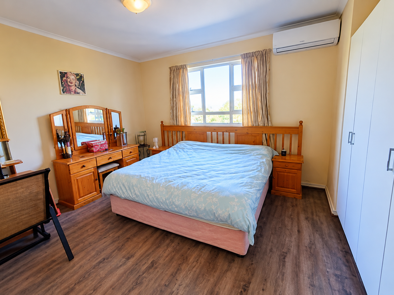 A well-maintained bedroom featuring laminate flooring, a built-in wardrobe, and a wall-mounted split-system air conditioner for climate control.