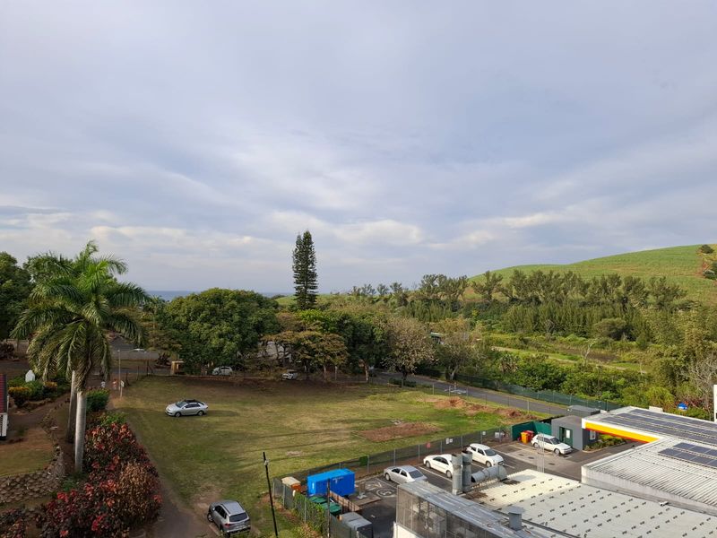 Elevated view overlooking a green landscape, trees, and nearby commercial infrastructure.