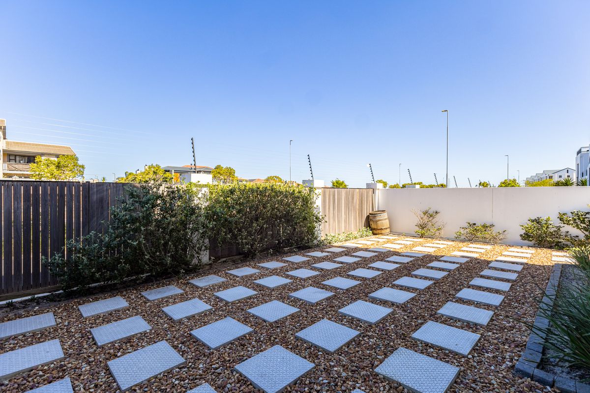 A low-maintenance rear garden featuring a gravel base with square paving stones, enclosed by timber fencing and boundary walls with electric security fencing.
