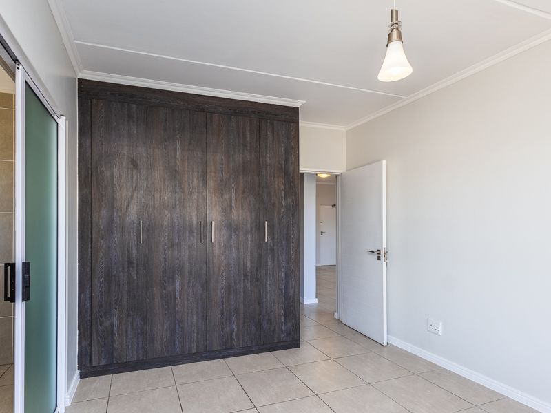 A bright, empty bedroom featuring dark wood-finish built-in cupboards, neutral tiled flooring, and a modern pendant light fixture.